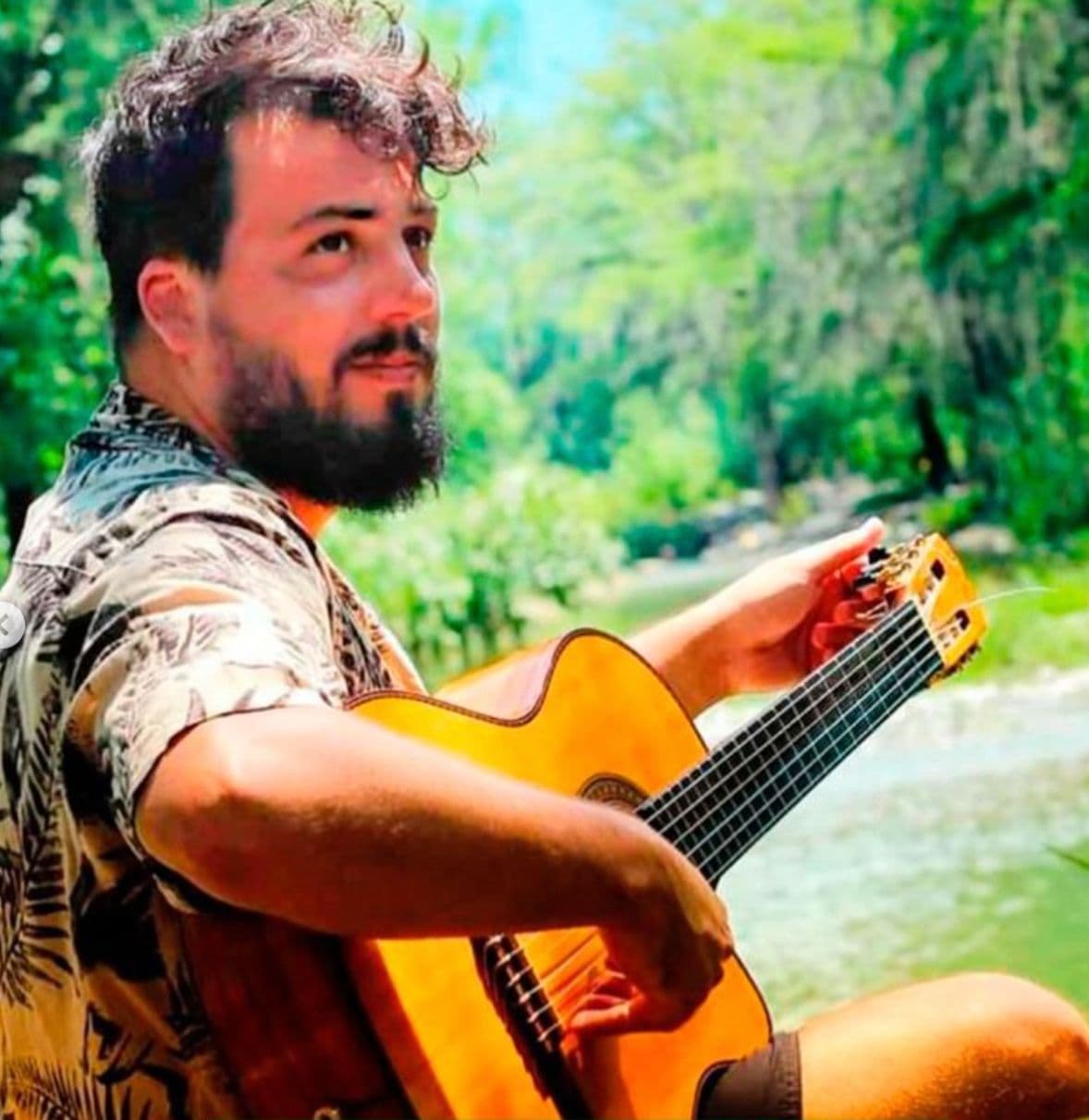 Rafa tocando la guitarra sentado junto a un río
