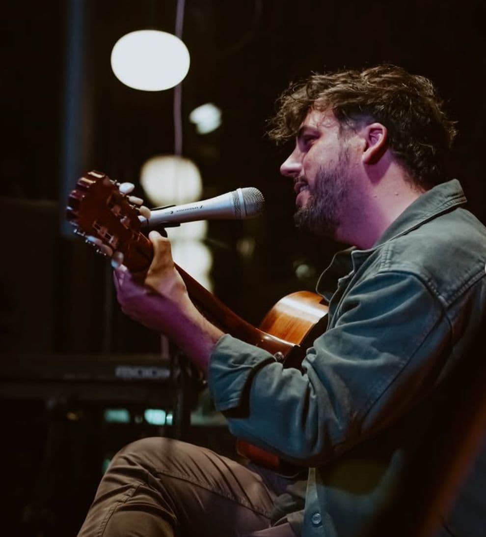 Rafa Doorish de perfil, sentado, cantando al micrófono con la guitarra