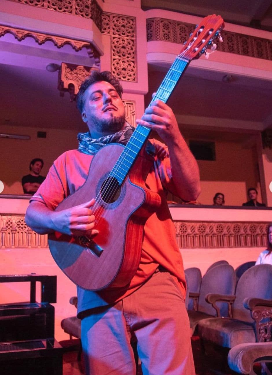 Rafa tocando de pie en un teatro, entre luces rojas y azules